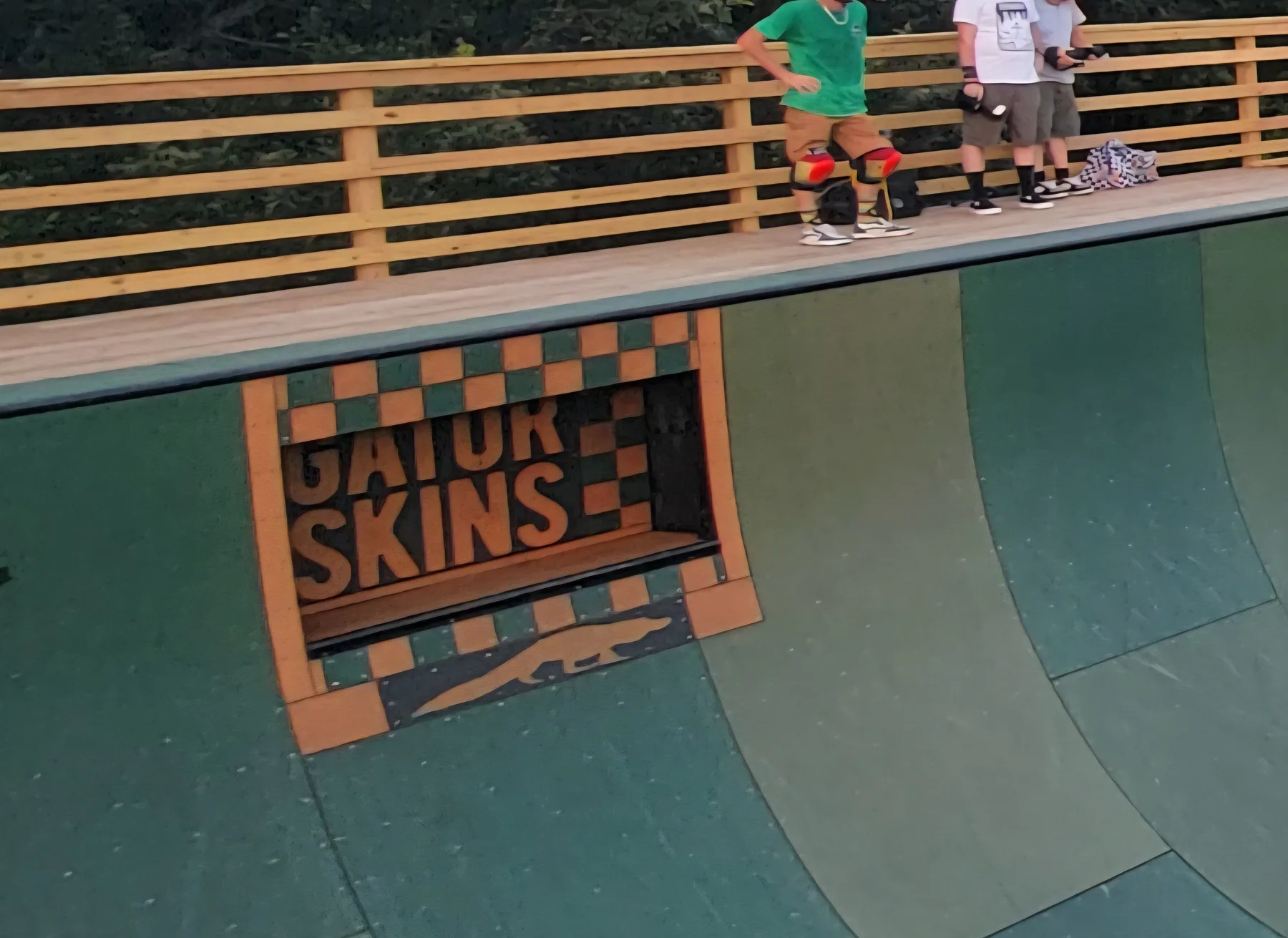 Skaters on the deck of Kona's rebuilt vert ramp above the Gator Skins logo